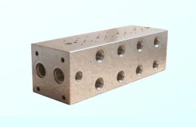 Machined bare metal 4-way hydraulic manifold block displaying multiple threaded connection ports.