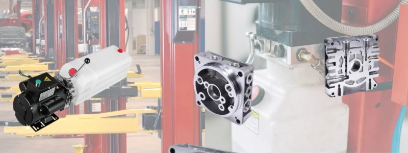 Components of an automotive lift hydraulic pump showing the motor, reservoir, and machined metal manifold block.